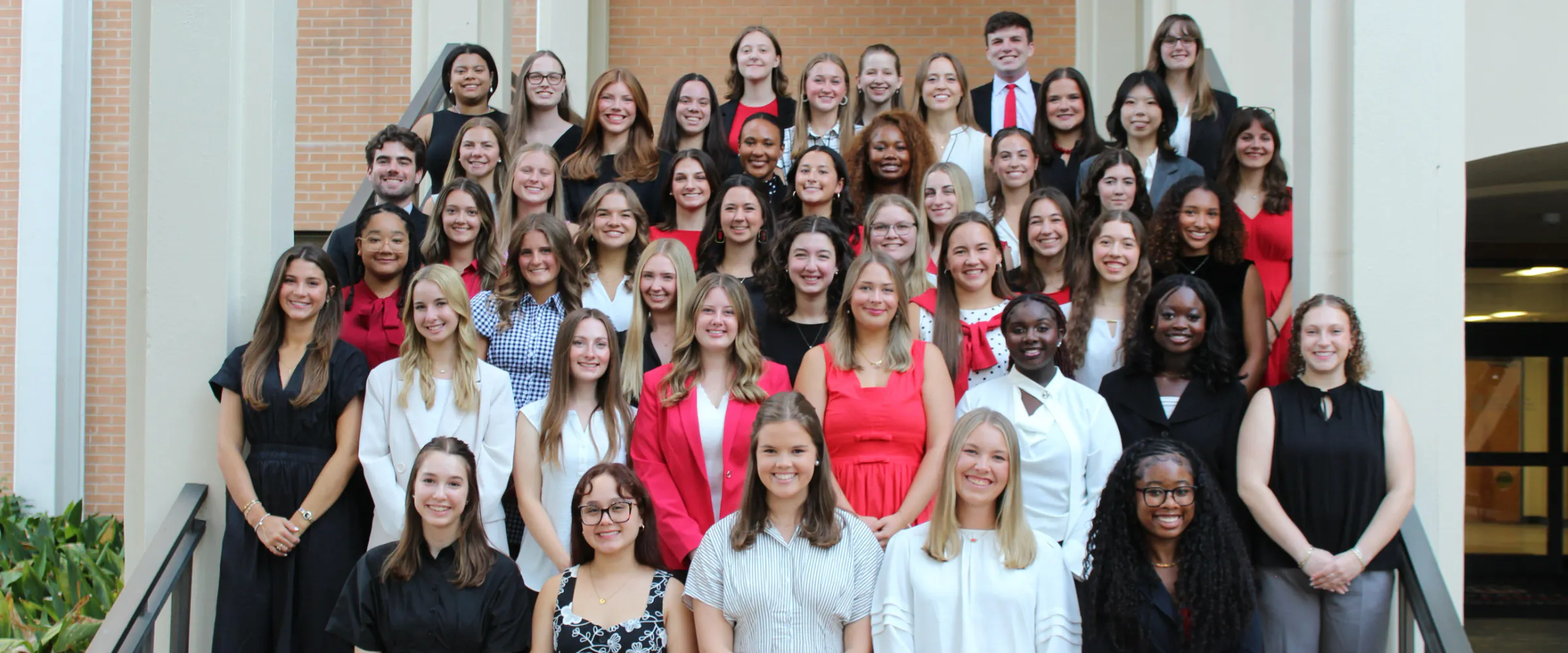 Group photo of Student Ambassadors in red, black, and white professional clothing on the Aderhold Hall stair case